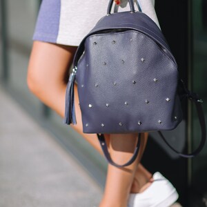May include: A dark blue leather backpack with silver studs and a tassel. The backpack has a zipper closure and adjustable straps.