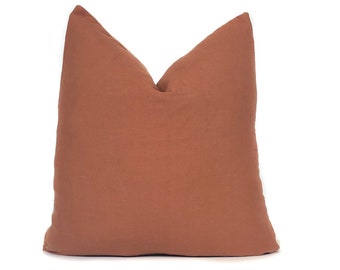 May include: A terracotta-colored throw pillow with a soft, linen texture. The pillow is square-shaped and has a simple, minimalist design.