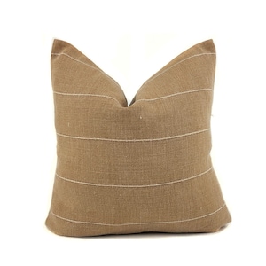 May include: A brown throw pillow with white stripes. The pillow is made of a textured fabric and has a simple, modern design.