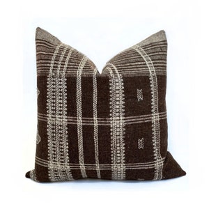 May include: A brown and white plaid pillow with a geometric pattern. The pillow is made of a soft, woven fabric.