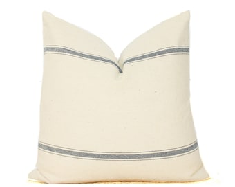 May include: A white pillow with two blue stripes across the front. The pillow is made of a soft, textured fabric.