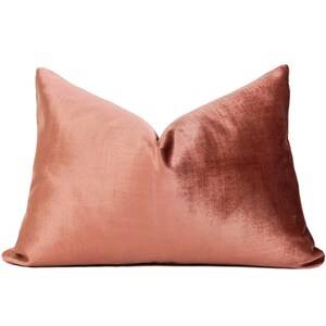 May include: A soft, blush-colored velvet pillow with a subtle sheen. The pillow is rectangular and has a simple, elegant design.