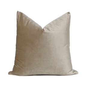 May include: A soft, plush, light brown throw pillow with a square shape and a subtle sheen.