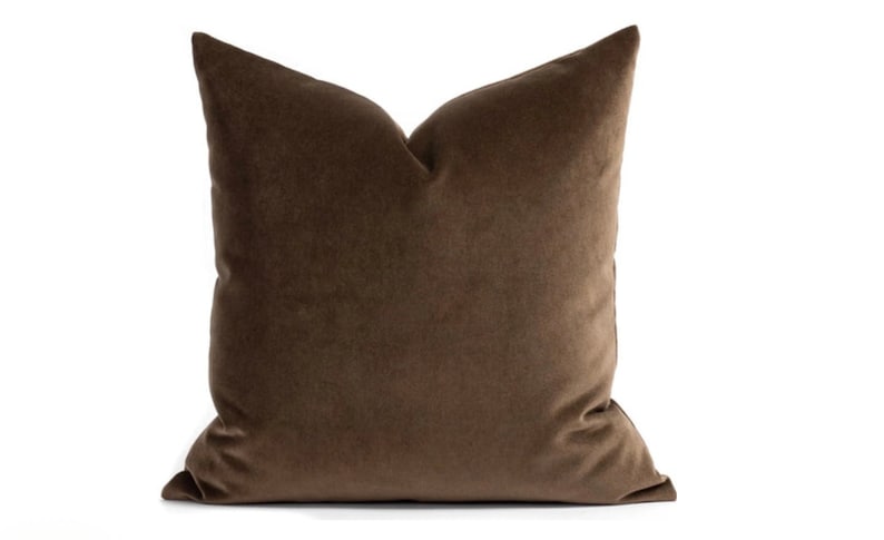 May include: A brown velvet pillow with a square shape. The pillow is made of a soft, plush fabric.