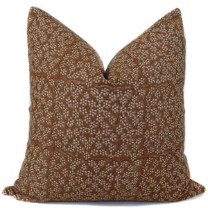 May include: A square decorative pillow with a brown background and a repeating pattern of small, off-white floral shapes. The pillow has a textured appearance and a stitched seam detail.