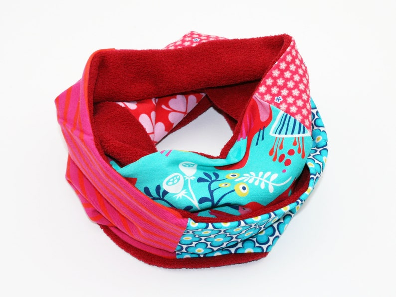 May include: A red, pink and blue patterned infinity scarf with a fleece lining.
