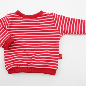 Può includere: Maglione a maniche lunghe a righe rosse e bianche con orlo e polsini a costine.