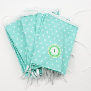 Könnte beinhalten: Ein blaues Stoffbanner mit weißen Sternen und einem grünen Kreis mit der Zahl "1" darauf. Das Banner besteht aus mehreren Stoffstücken, die mit weißen Schleifenbändern zusammengenäht sind.