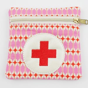 Può includere: Piccola pochette rettangolare con un motivo geometrico ripetuto rosa e arancione. Presenta un cerchio bianco con una croce rossa. Una cerniera dorata chiude la parte superiore.