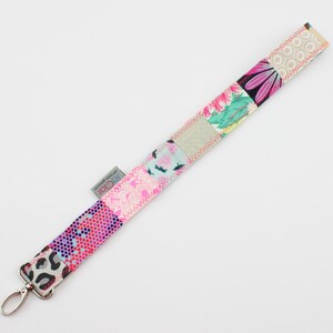 Könnte beinhalten: Ein farbenfroher Patchwork-Lanyard mit einem silbernen Schlüsselring. Der Lanyard besteht aus verschiedenen Stoffen mit floralen und geometrischen Mustern in Rosa, Blau, Grün und Weiß.