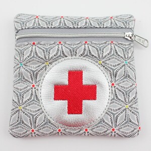 Può includere: Piccola pochette quadrata per kit di pronto soccorso con motivo geometrico grigio e cerniera argentata. La pochette presenta un'emblema a croce rossa su un cerchio argentato, ideale per riporre forniture mediche.