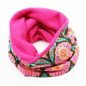 Könnte beinhalten: Ein leuchtend pinkfarbener Loop-Schal mit floralem Muster. Die Innenseite ist einfarbig, weich rosa, während die Außenseite einen braunen Hintergrund mit rosa, orangefarbenen und türkisfarbenen Blumenmustern aufweist. Dieses gemütliche Accessoire ist perfekt, um Farbe zu verleihen.