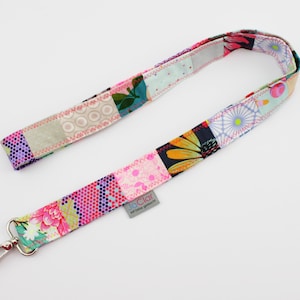 Può includere: Un laccio patchwork colorato con un moschettone argentato. Il laccio è realizzato con diversi tessuti con motivi floreali e geometrici. Il laccio ha un'etichetta che dice "laClar" e "always good vibes".