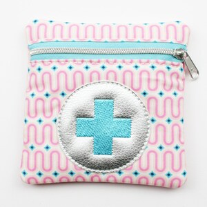 Può includere: Una piccola pochette con cerniera rosa e blu con un cerchio argentato e un segno più blu al centro. La pochette ha un motivo ripetitivo di linee ondulate rosa e blu.
