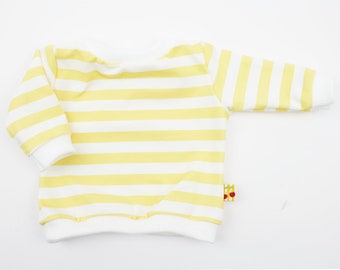 Puede incluir: Una sudadera de bebé a rayas amarillas y blancas. La camisa de manga larga tiene cuello redondo y puños y dobladillo blancos. Una pequeña etiqueta con un diseño de manzana roja está adjunta al costado.