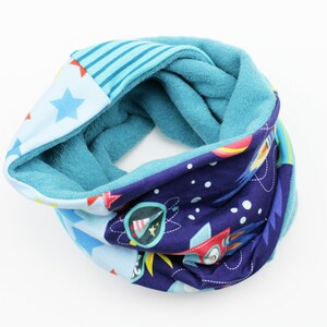 Könnte beinhalten: Ein blauer und lilafarbener Fleece-Halswärmer mit einem Weltraum-Motiv mit Raketen, Sternen und Planeten. Der Halswärmer ist reversibel mit einer einfarbigen blauen Fleece-Seite.