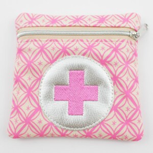 Può includere: Piccola pochette quadrata rosa e beige con cerniera e motivo geometrico ripetuto. Un cerchio color argento con una croce rosa è centrato sul davanti. La cerniera è argentata.