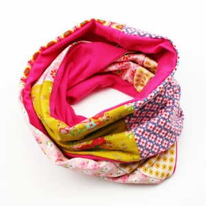 Könnte beinhalten: Ein pinkfarbener, gelber und blauer gemusterter Infinity-Schal aus Stoffresten. Der Schal ist zu einem Kreis gefaltet und bereit zum Tragen.