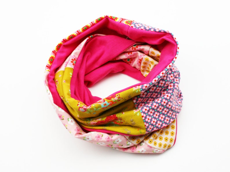 May include: A pink, yellow and blue patterned infinity scarf made from fabric scraps. The scarf is folded in a circle and is ready to be worn.