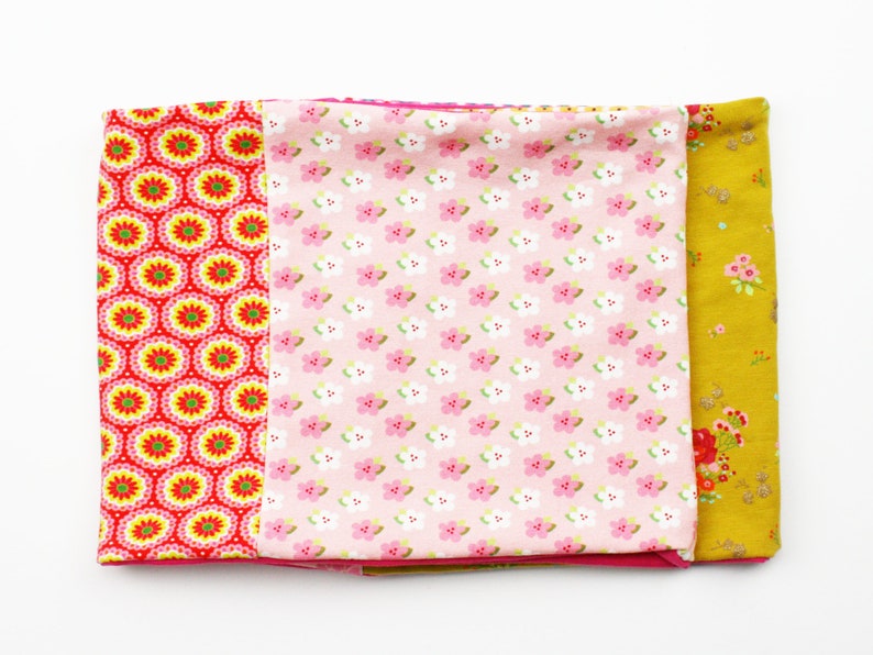 May include: A set of three fabric scraps with different patterns. The first scrap is red with yellow and white circles, the second is pink with white flowers, and the third is yellow with small brown flowers.