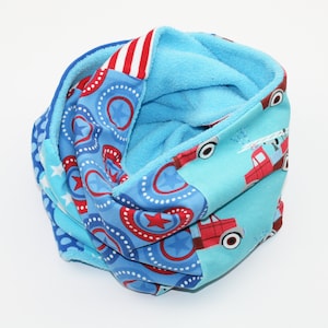 Könnte beinhalten: Ein blau-rot gemusterter Halsschlauch. Der Stoff zeigt Sterne, Kreise und Feuerwehrwagen-Motive. Die Innenseite ist hellblau. Ein warmes und bequemes Accessoire für kalte Tage.