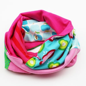 Könnte beinhalten: Ein pinkfarbener, blauer, grüner und roter Stoff-Halswärmer mit einem sich wiederholenden Muster aus Äpfeln und Streifen.