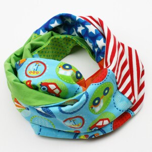 Könnte beinhalten: Ein farbenfroher Infinity-Schal aus Stoff mit verschiedenen Mustern. Eine Seite hat einen blauen Hintergrund mit weißen Sternen, eine andere Seite hat rot-weiße Streifen und die dritte Seite hat einen grünen Hintergrund mit weißen Punkten. Der Schal hat auch einen blauen Stoff mit einem Muster aus Autos und Flugzeugen.