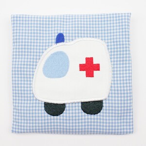 Könnte beinhalten: Ein blaues und weißes Karo-Stoffquadrat mit einem weißen gestickten Krankenwagen mit einem roten Kreuz an der Seite.