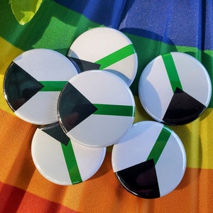 May include: Six round black, white, and green button pins with a green stripe and black triangle design. The pins are on a rainbow background.