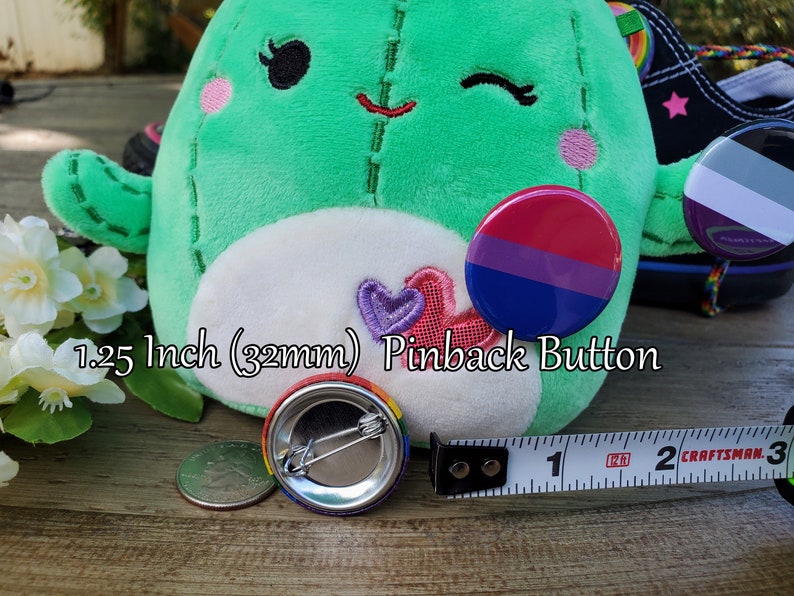 Puede incluir: Un bot&oacute;n de 32 mm (1,25 pulgadas) con un dise&ntilde;o de bandera del orgullo bisexual. El bot&oacute;n se muestra junto a una cinta m&eacute;trica para referencia de tama&ntilde;o.