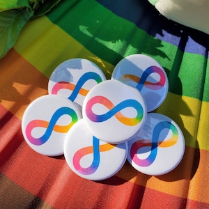 May include: Six round rainbow-colored buttons with an infinity symbol in the center. The buttons are arranged in a circle on a rainbow-colored fabric background.