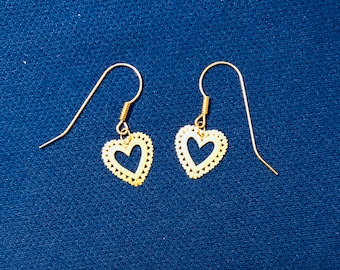 May include: A pair of gold heart-shaped earrings with a delicate, openwork design. The earrings have a simple, elegant style.