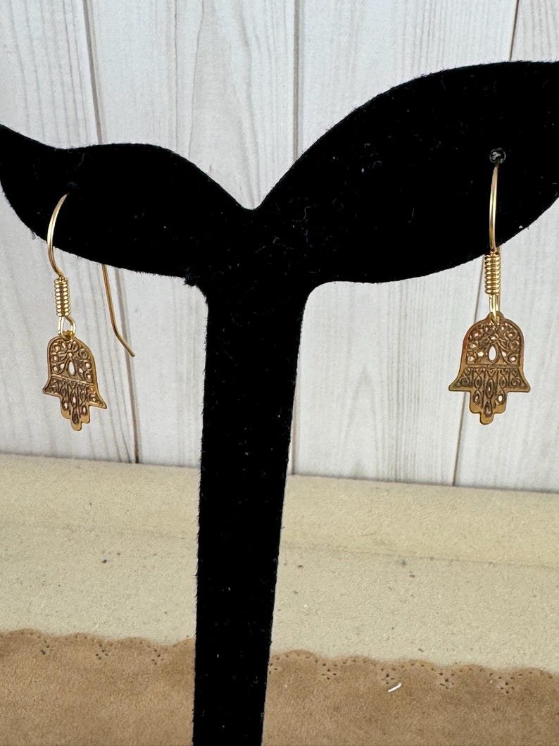 14 Karat Yellow Gold Hamsa Earrings with French Wires Hamsa is .625 in tall with Ear Wires 1.125 tall Shipped USPS Mail 
 The hamsa, or hamsa hand, is a talisman from the ancient Middle East. In its most common form, the amulet is shaped like a hand with three extended fingers in the middle and a curved thumb or pinky finger on either side. It is thought to protect against the “evil eye." It is most often displayed on necklaces or bracelets, and earrings
