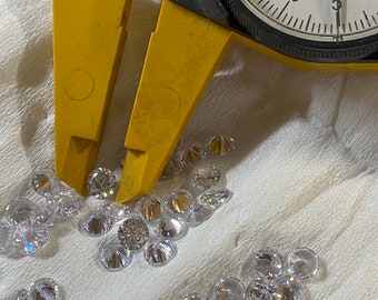 May include: A close-up of a yellow caliper measuring a pile of clear, faceted gemstones. The caliper reads 0.1 mm.
