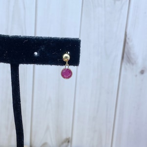 May include: A pair of gold stud earrings with a single pink gemstone dangling from each.