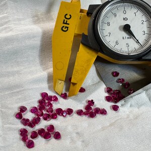 May include: A close-up of a yellow caliper measuring a pile of small, heart-shaped, pink gemstones. The caliper reads 0.1 mm.
