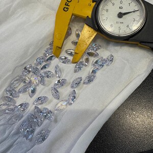 May include: A close-up of a set of clear marquise-shaped crystals, measured with a caliper. The caliper reads 0.1 mm.