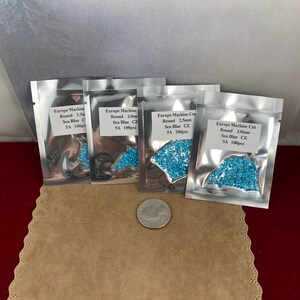 May include: Four small bags of blue round glass beads. Each bag has a label that says "Europe Machine Cut" and lists the size and quantity of the beads. The bags are on a brown surface.