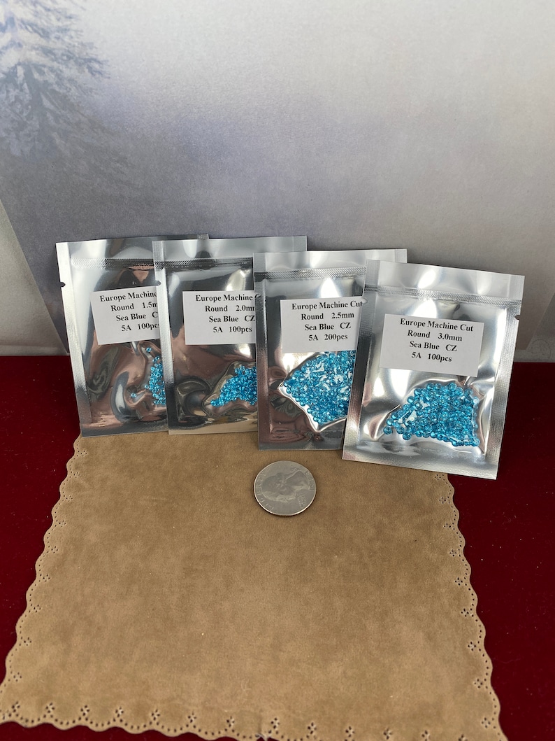 May include: Four small bags of blue round glass beads. Each bag has a label that says "Europe Machine Cut" and lists the size and quantity of the beads. The bags are on a brown surface.