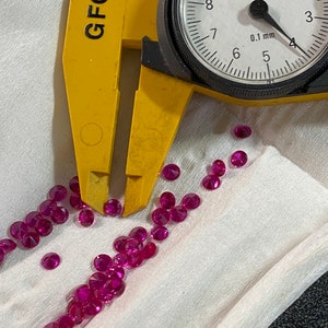 May include: A close-up of a yellow caliper measuring a pile of pink gemstones. The caliper reads 0.1 mm. The text "GFC" is visible on the caliper.