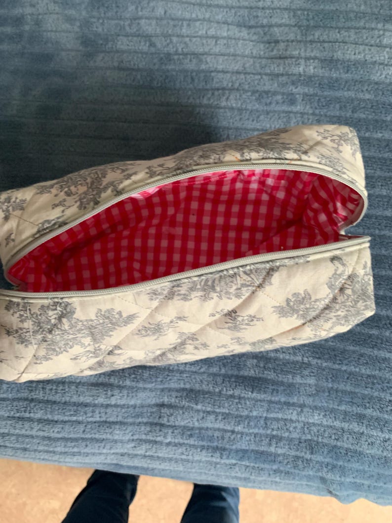 May include: A white quilted makeup bag with a floral pattern and a red and white gingham lining.