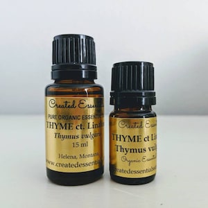 May include: Two amber glass bottles with black caps containing essential oil. The larger bottle is labelled "THYME ct. Linalool Thymus vulgaris 15 ml Created Essentials PURE ORGANIC ESSENTIAL OIL Helena, Montana www.createdessentials.com". The smaller bottle is labelled "THYME ct Linalool Thymus vulgaris Organic Essential Oil Created Essentials".