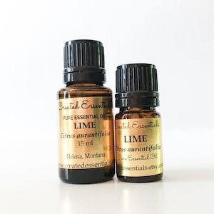 Op de afbeelding: Twee bruine glazen flessen limoen essentiële olie met zwarte doppen. De etiketten lezen "Created Essentials" en "LIME Citrus aurantifolia 15 ml". De flessen staan op een witte achtergrond.