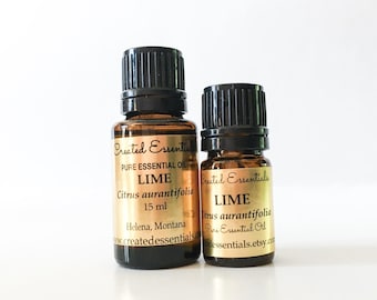 Può includere: Due bottiglie di vetro ambrato di olio essenziale di lime con tappi neri. Le etichette recitano "Created Essentials" e "LIME Citrus aurantifolia 15 ml". Le bottiglie sono su sfondo bianco.
