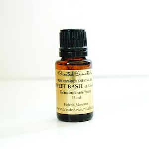 May include: A small amber glass bottle with a black cap. The label reads "SWEET BASIL" and "15 ml". The bottle is labeled "Created Essentials" and "Pure Organic Essential Oil".