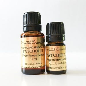 May include: Two amber glass essential oil bottles with black caps. The labels read "Created Essentials" and "PATCHOULI" with the botanical name and volume. The text "Helena, Montana" is also visible.