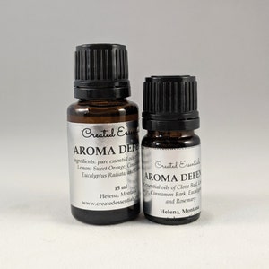 May include: Two amber glass bottles with black caps, labeled "Created Essentials" and "Aroma Defen". The larger bottle is 15 ml and the smaller bottle is 10 ml. Both bottles are labeled with the text "Helena, Montana" and a website address.