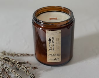 Puede incluir: Una vela en un frasco de vidrio ámbar cilíndrico con cera blanca y una mecha de madera. La etiqueta dice: lavender SANDALWOOD, HAND POURED 8OZ, NATURAL SOY WAX, WOOD WICK COLLECTION, Cozy Light candle co. Ramitas de lavanda seca se encuentran junto al frasco.