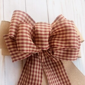 May include: A large red and tan gingham bow with a burlap ribbon tail. The bow is tied in a classic style with a center loop and two side loops.