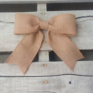 May include: A large, brown burlap bow tied with a simple knot. The bow is displayed against a light wood background.